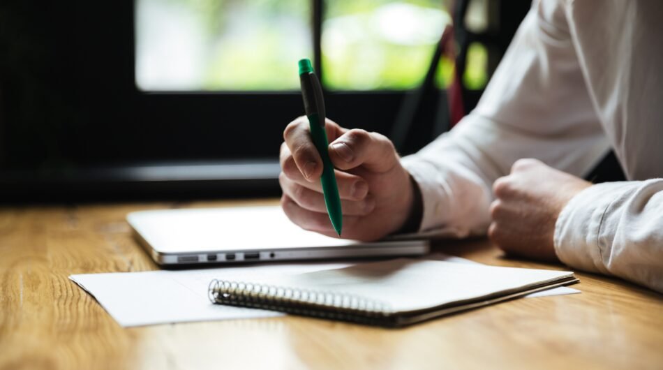 cropped-photo-mans-hand-holding-green-pen-while-taking-notes-1