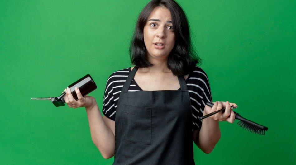 young-beautiful-female-hairdresser-apron-holding-scissors-spray-brush-confused-standing-green-wall-1